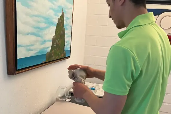 Umzugshelfer in grünem Poloshirt packt ein Glas in ein Papier vor einer Wand mit einem Bild