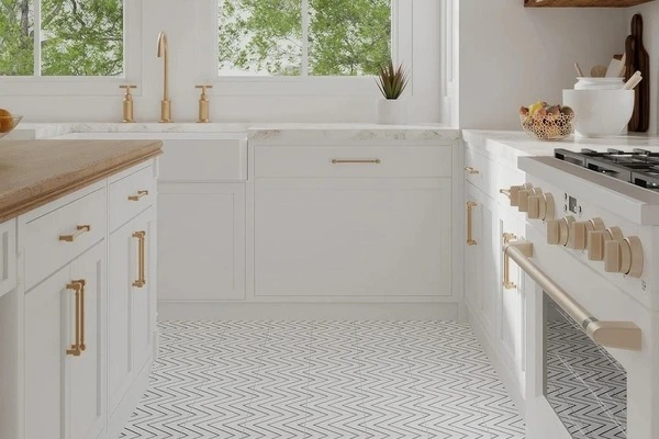 Weiße Küche mit goldfarbenen Griffen, großem Fenster, Spüle unter dem Fenster und gemustertem Boden.