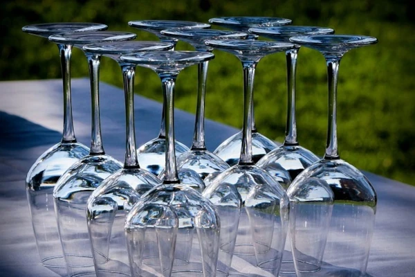 Mehrere umgedrehte Weingläser stehen dicht nebeneinander auf einer weißen Oberfläche vor unscharf grünem Hintergrund