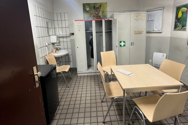 KVB-Pausenraum mit Tisch, vier Stühlen, Spülbecken, Schließfächern und zwei Tierpostern an den Wänden