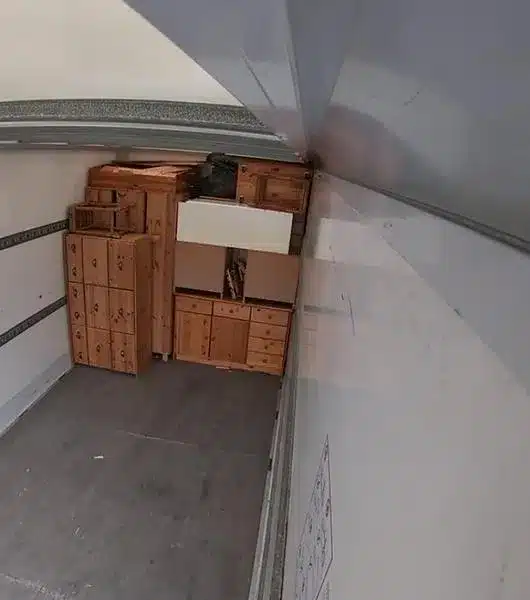 Innenraum eines Lkw mit mehreren gestapelten Holzmöbeln und Kartons am hinteren Ende