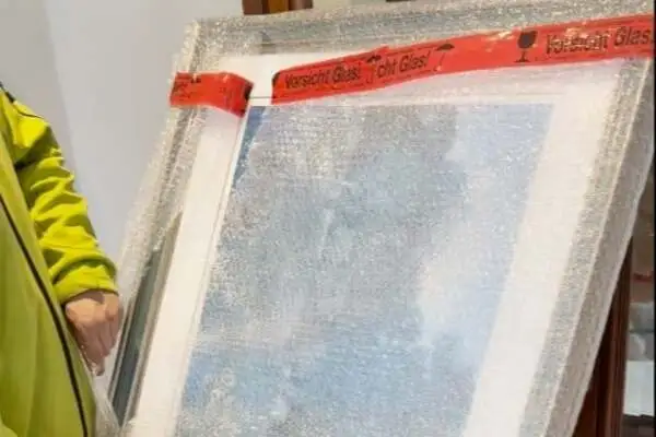 Bild, das mit Luftpolsterfolie und rotem Warnband mit der Aufschrift 'Vorsicht Glas' geschützt wird