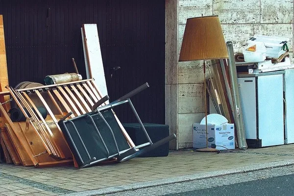 Verschiedene sperrige Möbelstücke und Haushaltsgegenstände vor einem Haus an einer Wand gestapelt