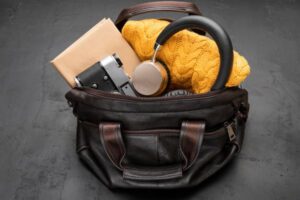 Handtasche, aus der Kopfhörer, eine Kamera, ein Notizbuch und eine Decke herausschauen