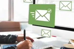 Eine Person sitzt an einem PC. Davor blopenn E-Mail-Symbole im Bild auf.