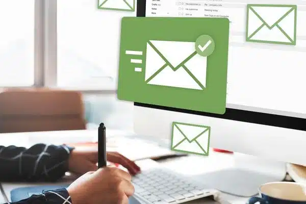 Eine Person sitzt an einem PC. Davor blopenn E-Mail-Symbole im Bild auf.