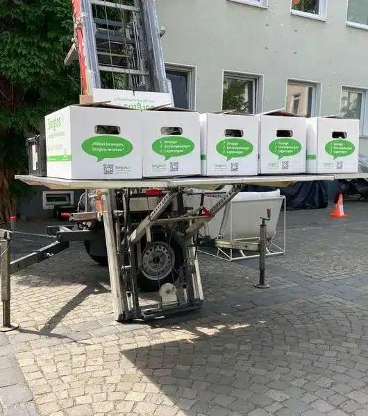 Mehrere Umzugskartons der Firma Sorglos Umzüge & Entrümpelungen stehen auf der Plattform eines Außenlifts.