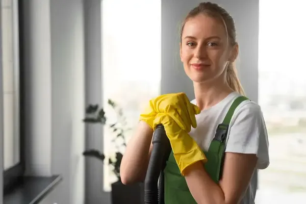 Gebäudereinigungskraft hält den Saugschlauch eines Staubsaugers in der Hand und lächelt in die Kamera.
