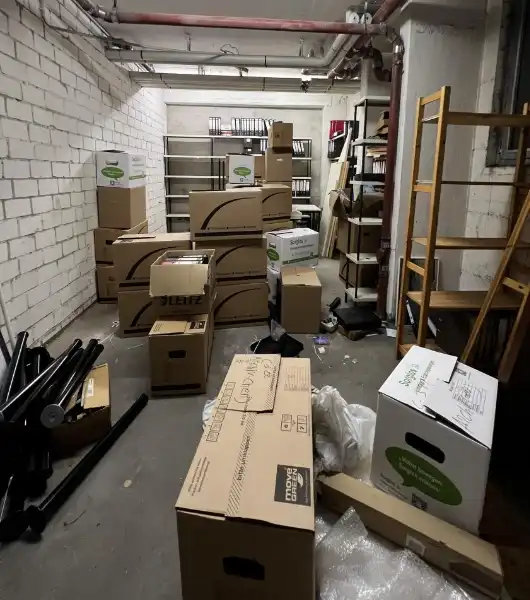 Kellerraum mit weißen Ziegelwänden, gefüllt mit gestapelten Umzugskartons und Regalen aus Holz und Metall.