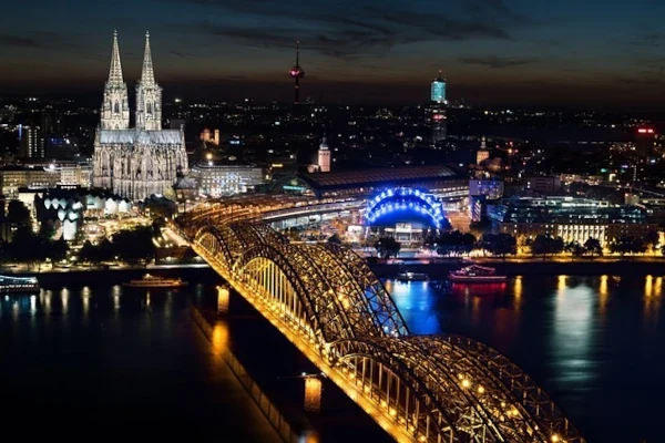 Beleuchtete Hohenzollernbrücke über den Rhein mit Kölner Dom und Stadt bei Nacht.