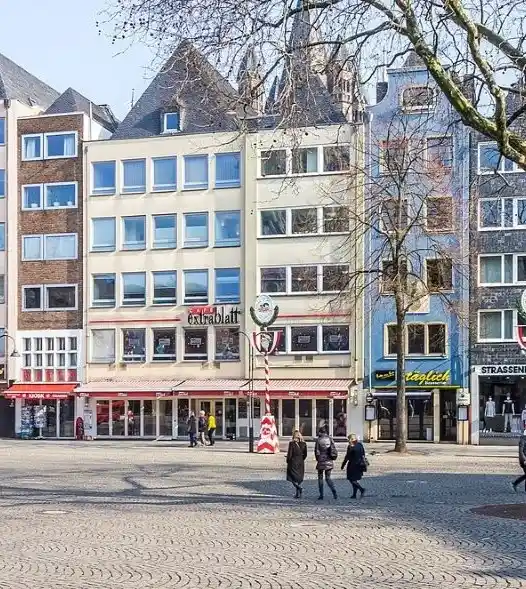 Mehrere mehrstöckige Gebäude mit Geschäften im Erdgeschoss am alten Markt in Köln mit wenigen Passanten und kahlen Bäumen