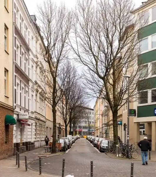 Blick in eine enge Straße in Köln Kalk mit geparkten Autos und kahlen Bäumen zwischen mehrstöckigen Wohngebäuden.