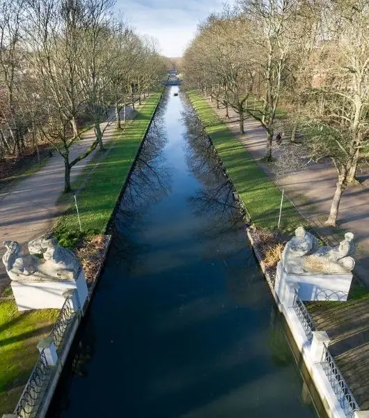 Blick von einer Brücke auf einen geraden Kanal in Lindenthal mit beidseitigen Wegen und kahlen Bäumen.