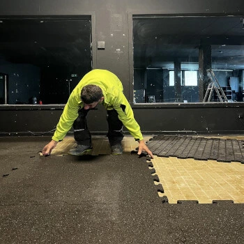 Entrümpler in grüner Jacke kniet auf dem Boden und entfernt ineinandergreifende Bodenplatten