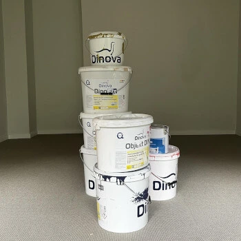 Mehrere übereinander gestapelte weiße Farbeimer mit der Aufschrift 'Dinova' in einem leeren Raum