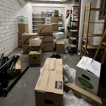 Kellerraum mit gestapelten Umzugskartons, Regalen und verstreuten Gegenständen