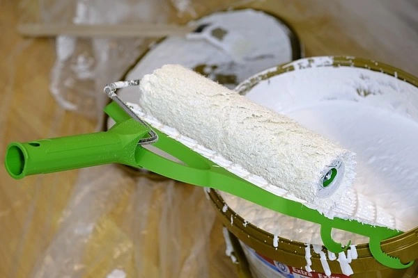 Farbroller mit grünem Griff liegt auf einem Farbeimer mit weißer Farbe