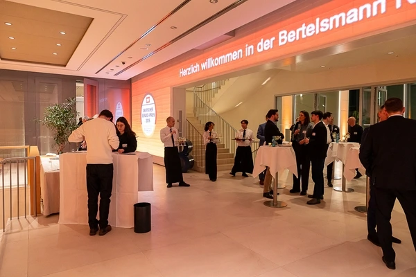 Mehrere Personen stehen im modernen Empfangsbereich mit Stehtischen in der Bertelsmann-Repräsentanz in Berlin