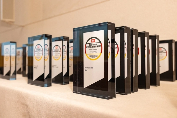 Mehrere rechteckige Glastrophäen mit der Aufschrift 'Deutscher Service-Preis 2020' stehen in einer Reihe auf einem hellen Tuch.