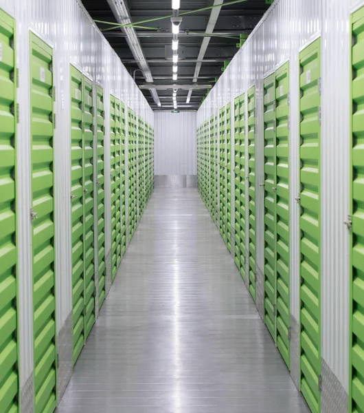 Langer Gang zwischen zwei Reihen von grünen Lagerboxen in einer hellen Lagerhalle