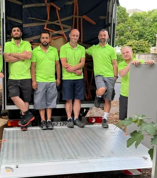 Fünf Sorglos-Umzugshelfer in grünen Poloshirts stehen entspannt auf der Ladefläche eines Umzugstransporters, im Hintergrund gepolsterte Möbelstücke im Transporter