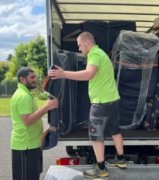 Zwei Sorglos-Umzugshelfer in grünen Poloshirts laden gepolsterte Möbel in denLkw
