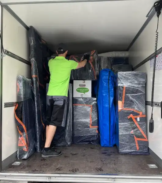 Sorglos-Umzugshelfer in grünem Arbeitsshirt lädt verpackte Möbel und Kartons in den Umzugstransporter