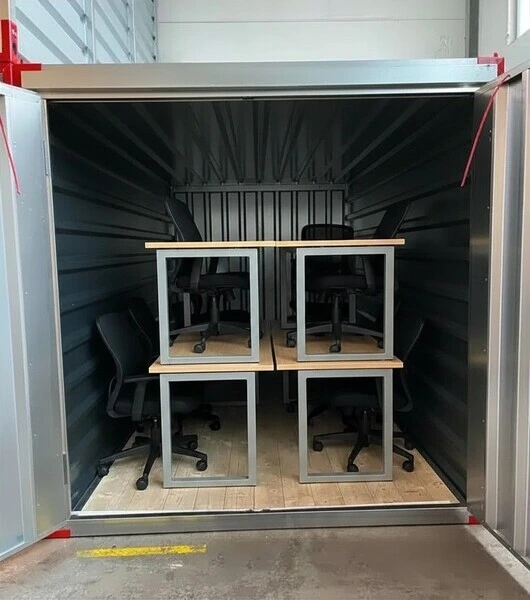 Mehrere Bürostühle mit Rollen und Schreibtische stehen in einem offenen Lagercontainer